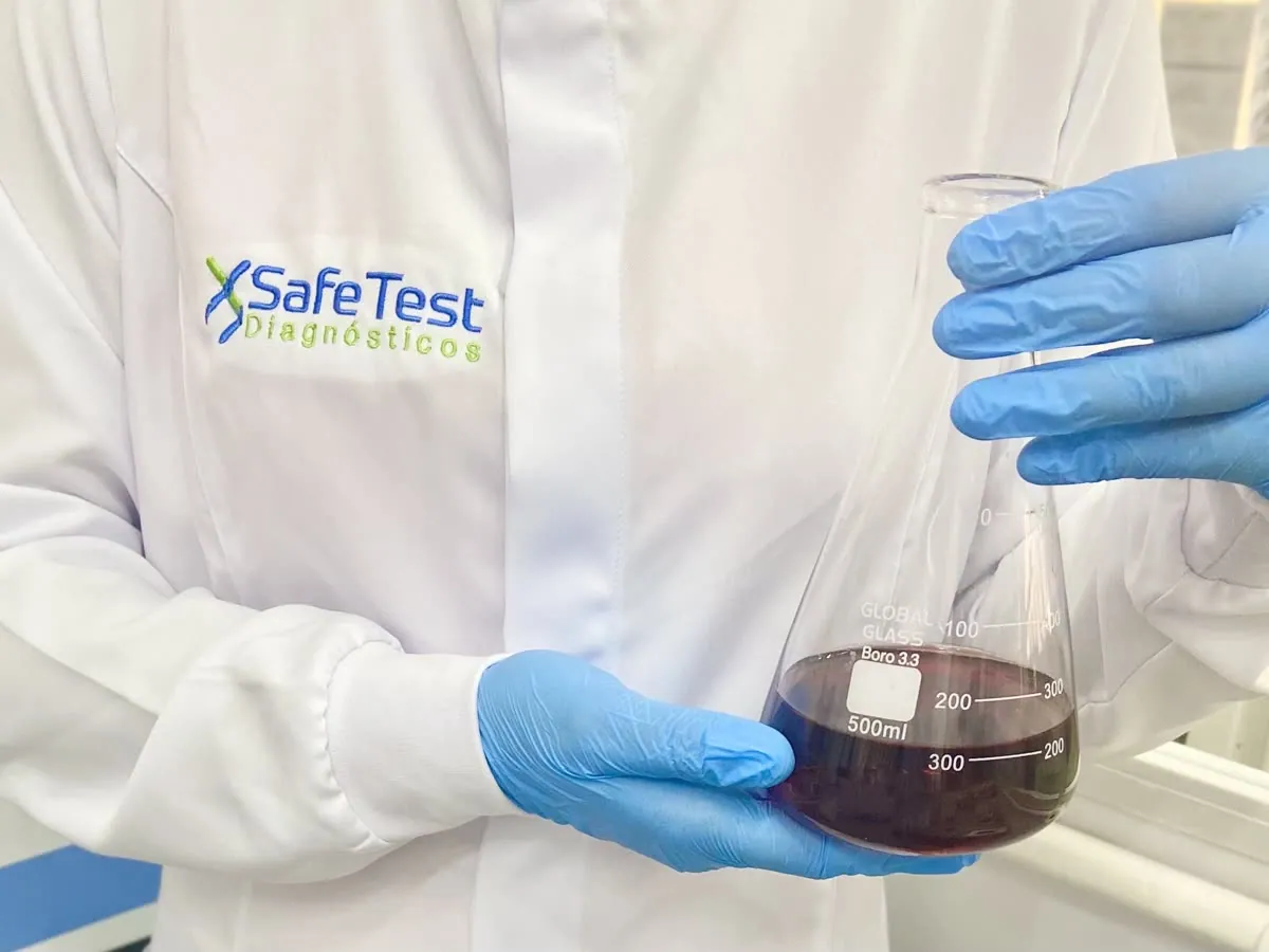 Professional in a lab coat with the SafeTest Diagnósticos logo holding a laboratory flask